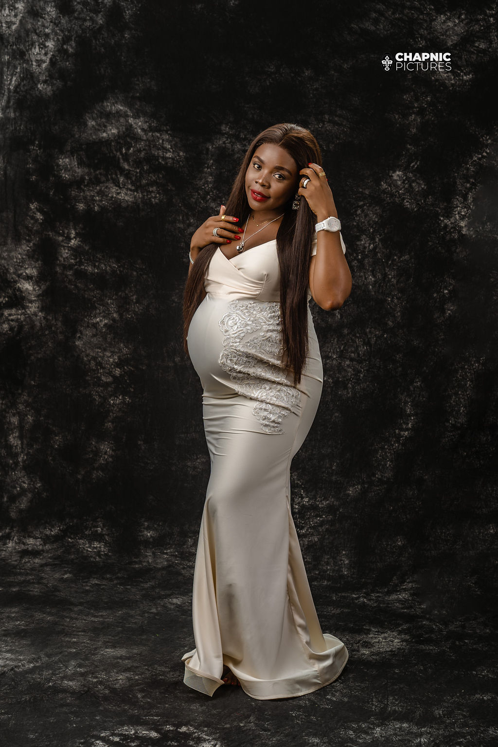 A maternity portrait in a flowing ivory dress against a dark studio backdrop - Chap Nic Pictures
